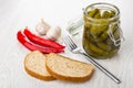 Marinated gherkins in glass jar, fork, garlic, chili peppers, bread on table