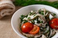 Marinated oyster mushrooms, garnished with cherry tomatoes and green dill. A dish with onions and butter in a white plate with