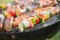 Marinated pork neck steak meat and colorful vegetable skewers roasting on kettle barbecue grill with charcoal and smoke in garden Royalty Free Stock Photo