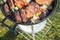 Marinated pork neck steak meat and colorful vegetable skewers roasting on kettle barbecue grill with charcoal and smoke in garden Royalty Free Stock Photo