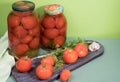 Marinated tomatoes in jars . Fresh tomatoes on a wooden chopping Board with garlic and herbs.