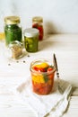 Marinated tomatoes in open glass jar, assorted vegetable preserves on white background. Vertical image.