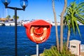 View on lifebelt in red box with palm tree and street light in mediterranean Harbour. Boats and blue sky background