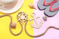 Marine paraphernalia and beach accessories. Wooden steering wheel and an anchor with a rope on a bright pink and yellow background