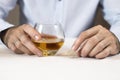 Marital problems. Hands of a man sitting at a white table are holding a glass of whiskey. The other hand is holding a wedding