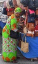 Market stall trader in colorful outfit selling handbags.