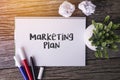 Marketing Plan word with Notepad and green plant on wooden background.
