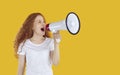 Expressive girl using megaphone to announce discounts and sales isolated on yellow background.