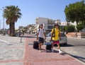 Marmari, Evia island, Greece. August 2020: Two male tourists walk with suitcases and a tent along the promenade of the resort town