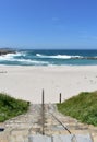 Beach with stone stairs, white sand and wild sea with waves, foam, and blue sky. A Marosa Beach, Burela, Lugo, Galicia, Spain. Royalty Free Stock Photo