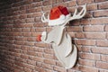 Marquetry deer hanging on the wall with santa claus hat and red nose. Christmas decoration Royalty Free Stock Photo