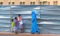 Veiled Muslim woman with three children in front of corrugated metal fence at construction site