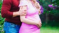 A married couple hugs against a blossoming lilac. the husband hugs the Pregnant wife