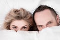 Married couple, man and woman, are lying in bed, hugging and sleeping on white bedding. Hiding their faces under blanket Royalty Free Stock Photo