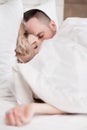 Married couple, man and woman, are lying in bed, hugging and sleeping on white bedding. Hiding their faces under blanket Royalty Free Stock Photo