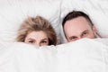 Married couple, man and woman, are lying in bed, hugging and sleeping on white bedding. Hiding their faces under blanket Royalty Free Stock Photo