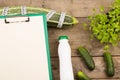 marrow squash, measure tape, blank clipboard, bottle of water and cucumbers on brown wooden table Royalty Free Stock Photo