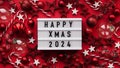 Marry Christmas banner concept. White board with text Happy Xmas 2024 among christmas red decor, balls, berries,striped candy