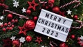 Marry Christmas banner concept.White board with text Happy Xmas 2023 among Christmas red decor,balls,berries, striped candy canes,