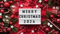 Marry Christmas banner concept.White board with text Happy Xmas 2024 among Christmas red decor,balls,berries, striped candy canes, Royalty Free Stock Photo