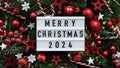 Marry Christmas banner concept.White board with text Happy Xmas 2024 among Christmas red decor,balls,berries, striped candy canes,