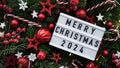 Marry Christmas banner concept.White board with text Happy Xmas 2024 among Christmas red decor,balls,berries, striped candy canes,