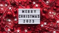 Marry Christmas banner concept. White board with text Marry Christmas 2023 among christmas red decor, balls, berries,striped candy Royalty Free Stock Photo