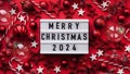 Marry Christmas banner concept. White board with text Marry Christmas 2024 among christmas red decor, balls, berries,striped candy