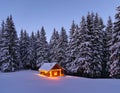 Marry Christmas and New Year. Wooden hut on the lawn covered with snow. The lamps light up the house at the evening time. Winter Royalty Free Stock Photo