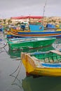 Few colourful traditional Maltese fishing boat Luzzu anchored with old houses behind at cloudy fishing village Marsaxlokk, Malta Royalty Free Stock Photo