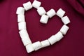Marshmallows laid out in the shape of a heart isolated on a pink background. Bunch of small white marshmallows laid out in the for