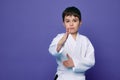 Martial arts attack. School age boy aikido fighter in white kimono over purple background with copy space for advertising