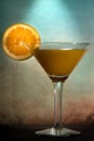 Martini glass with a mix of orange juice and alcohol with a slice of orange fruit against dark and moody orange blue background Royalty Free Stock Photo