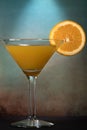 Martini glass with a mix of orange juice and alcohol with a slice of orange fruit against dark and moody orange blue background Royalty Free Stock Photo