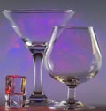 Martini Glass together with Cognac Glass and ice cubes with flashing smooth violet lights on background