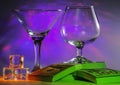 Martini Glass together with Cognac Glass on a packs of the 100s of us dollars and ice cubes with flashing bright violet lights on Royalty Free Stock Photo