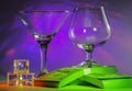 Martini Glass together with Cognac Glass on a packs of the 100s of us dollars and ice cubes with flashing bright violet lights on Royalty Free Stock Photo