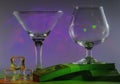 Martini Glass together with Cognac Glass on a packs of the 100s of us dollars and ice cubes with flashing smooth violet lights on Royalty Free Stock Photo