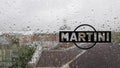 Martini sticker logo. A brand of Italian-made vermouths and sparkling wines. Water drop on glass window during rain with blurred