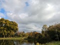 Marvel at the dynamic beauty of the sky above the city park\'s serene lake. Royalty Free Stock Photo