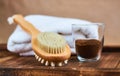 Masage brush, body skin care and coffee natural scrub in glass, white towel and greens on dark wooden background.