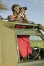 Masai scout with binoculars looks for animals from a Landcruiser during a tourist game drive at the Lewa Wildlife Conservancy in