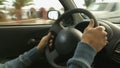 Masculine man's hands firmly holding steering wheel of car riding around city