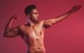 Masculine man standing shirtless with his fist closed and showing fighting technique while posing against a red studio