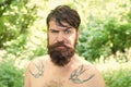 The masculine nature. Masculine guy with tattoo on shoulders on summer landscape. Bearded man shirtless with masculine Royalty Free Stock Photo