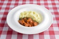 Mashed potato with gravy poured over. Served in a white plate over red plaid table cloth Royalty Free Stock Photo