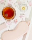 Mask for sleep, cup of tea, candle and rose petals on a white wooden tray