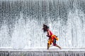 Masked Bujang Ganong dancer wields a whip in front of textured falling waterp Royalty Free Stock Photo