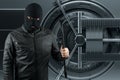 Masked burglar with crowbar in the background. Bank vault doors, large safe, bank robbery. The concept of deposit protection,