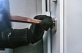 Masked burglar with crowbar breaking and entering into a victim  home Royalty Free Stock Photo